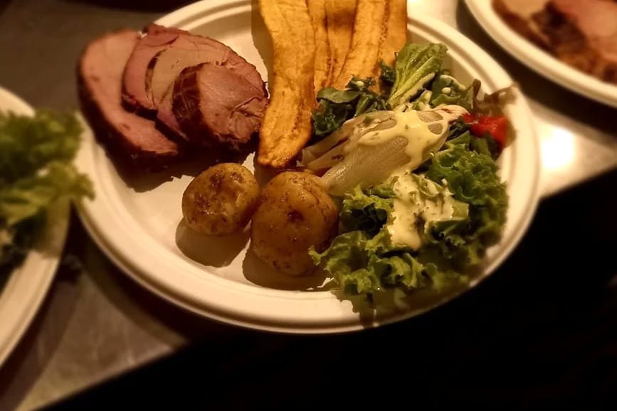 Platos con jamón y costillas ahumadas, tajadas de plátano maduro, papas y ensalada, servidos de noche.