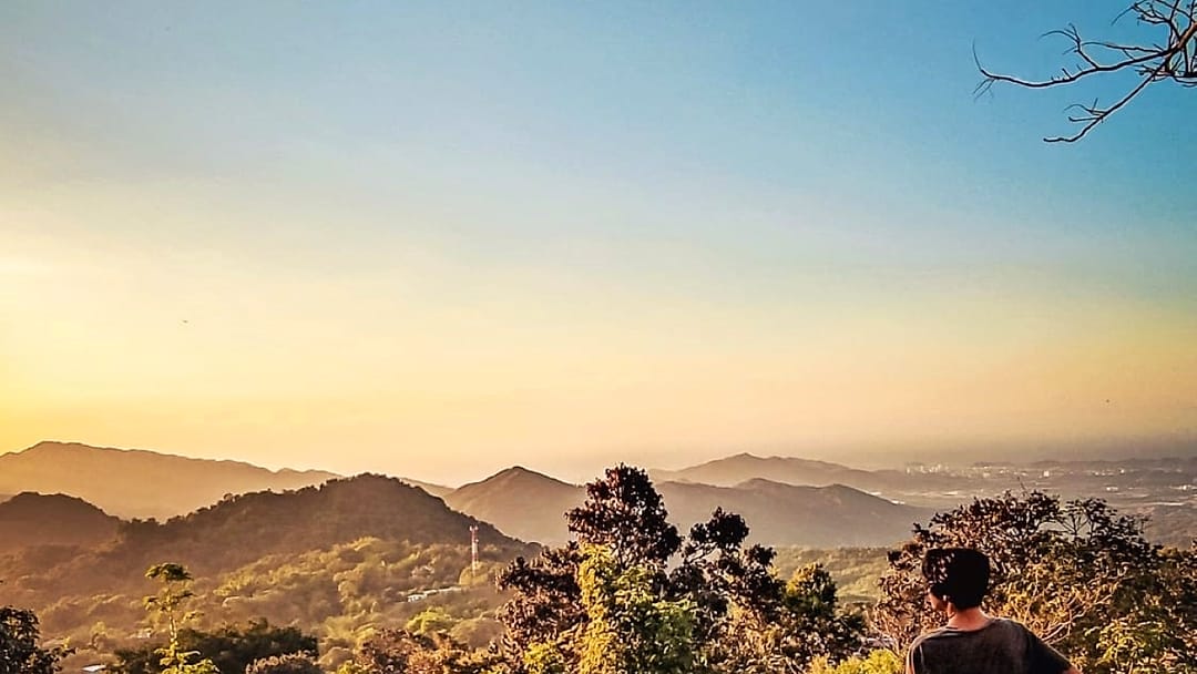 Una persona de pie sobre una roca del mirador privado mira las lomas de la Sierra Nevada encendidas por la luz dorada del atardecer.