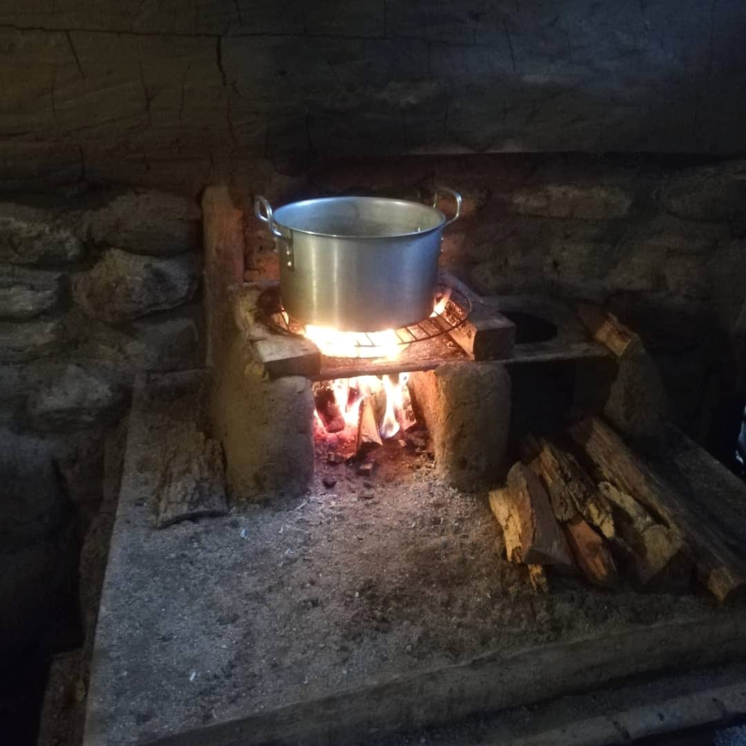 Una olla de aluminio sobre un fogón de leña construido con piedra y barro.
