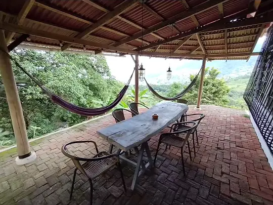 Terraza techada con hamacas y mesa larga frente al valle.