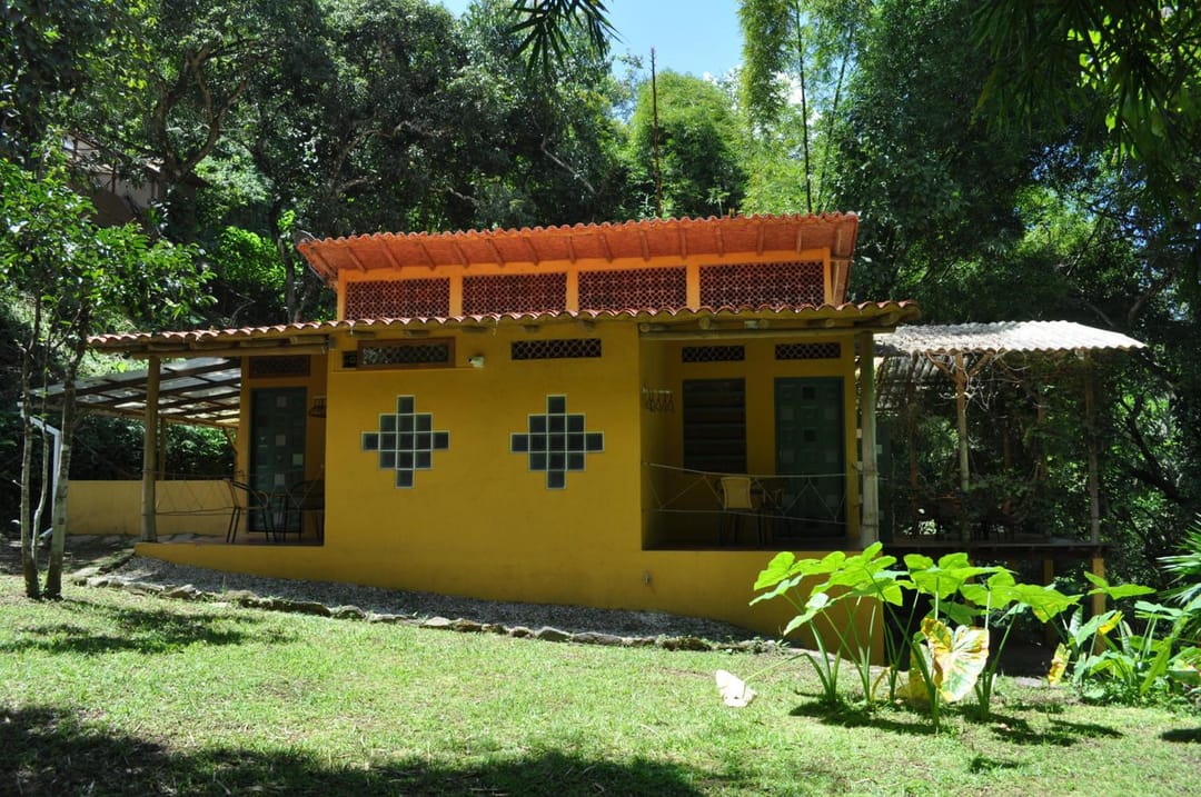 Fachada amarilla con ventanas de cuadros de vidrio azul, techo de teja y prado verde.