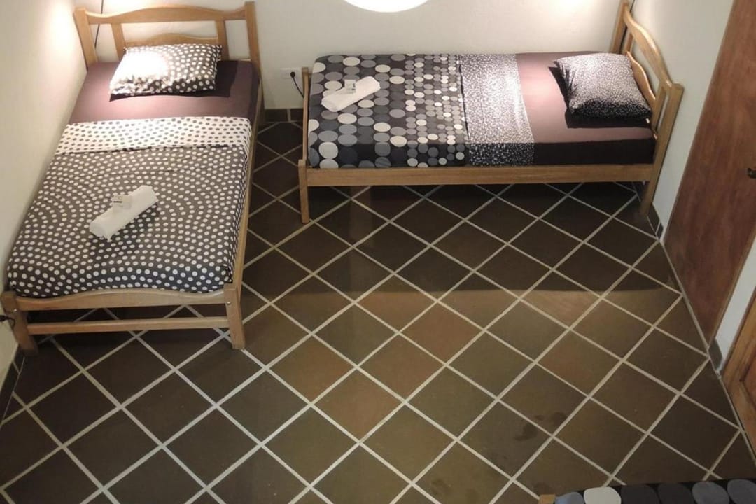 Lado del dormitorio con dos camas sencillas de colchas de puntos y lámpara de papel.