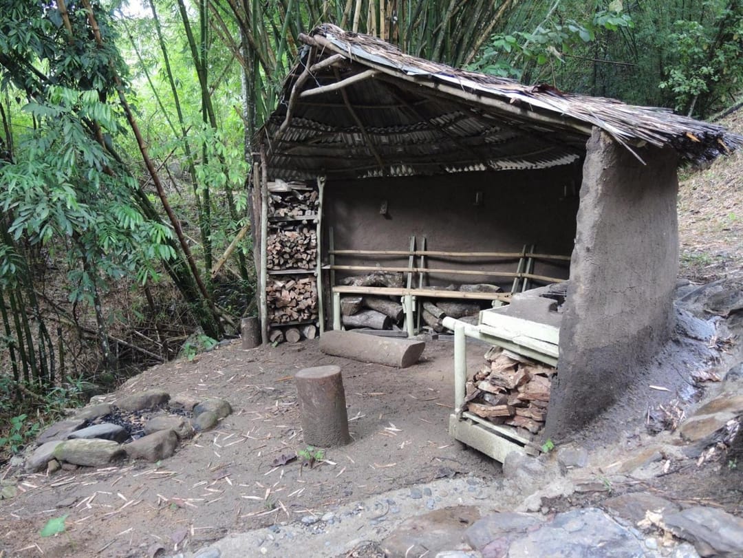 Kiosko rústico con fogón y parrilla entre guaduas, con leña apilada.