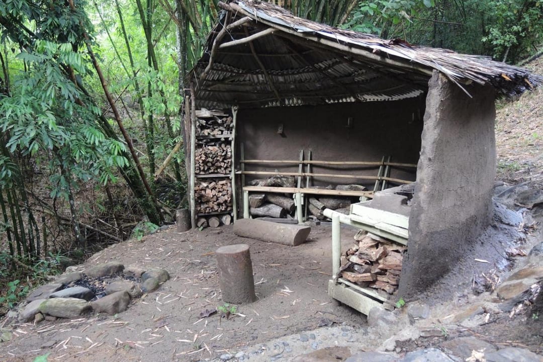 Kiosko rústico con fogón y parrilla entre guaduas, con leña apilada.