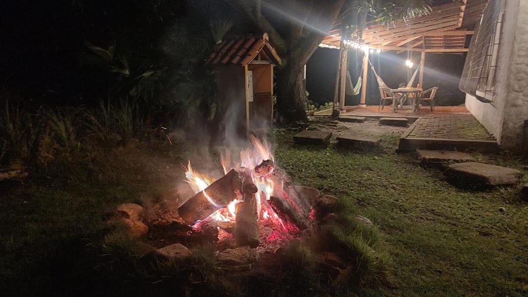 Una fogata de noche en el prado, con la barra iluminada al fondo.