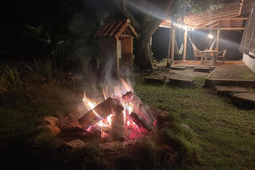 Una fogata de noche en el prado, con la barra iluminada al fondo.