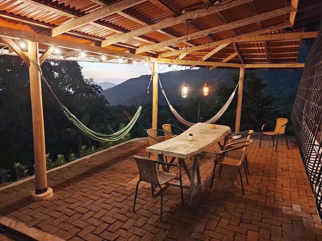 La terraza al anochecer con luces colgantes, hamacas y la mesa larga lista.