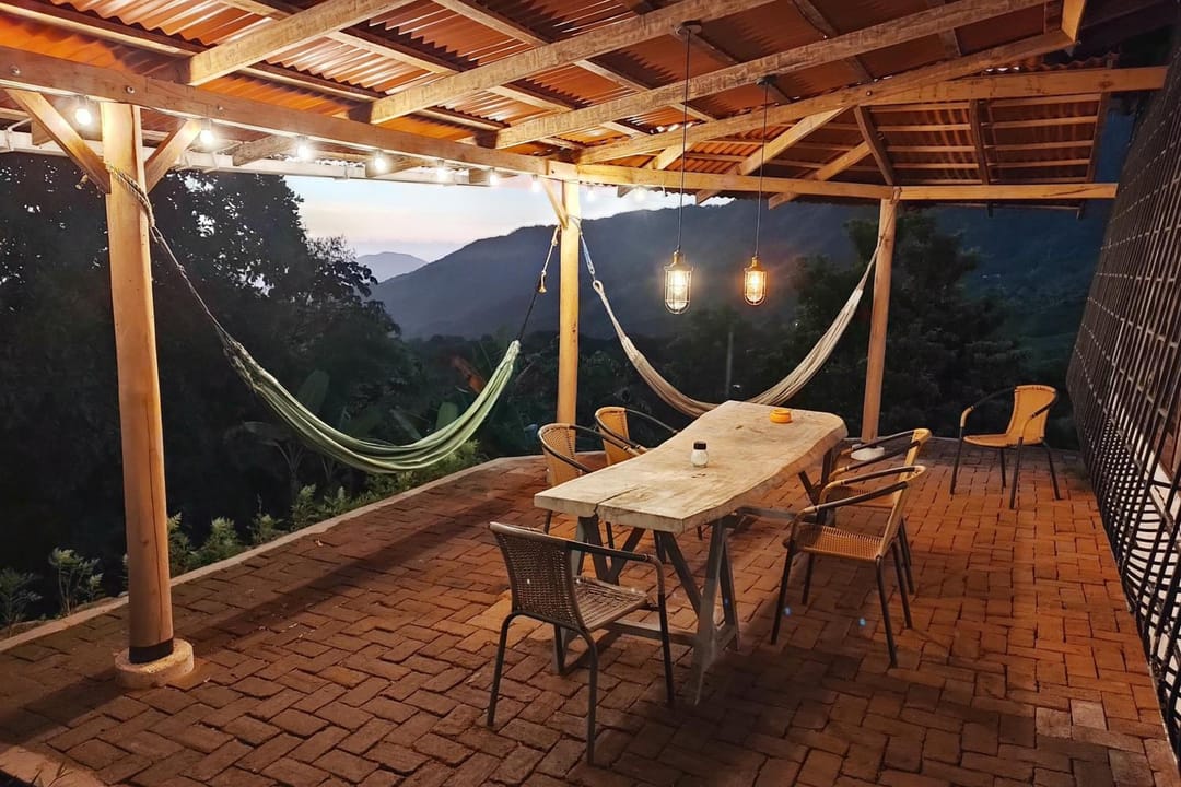 La terraza al anochecer con luces colgantes, hamacas y la mesa larga lista.