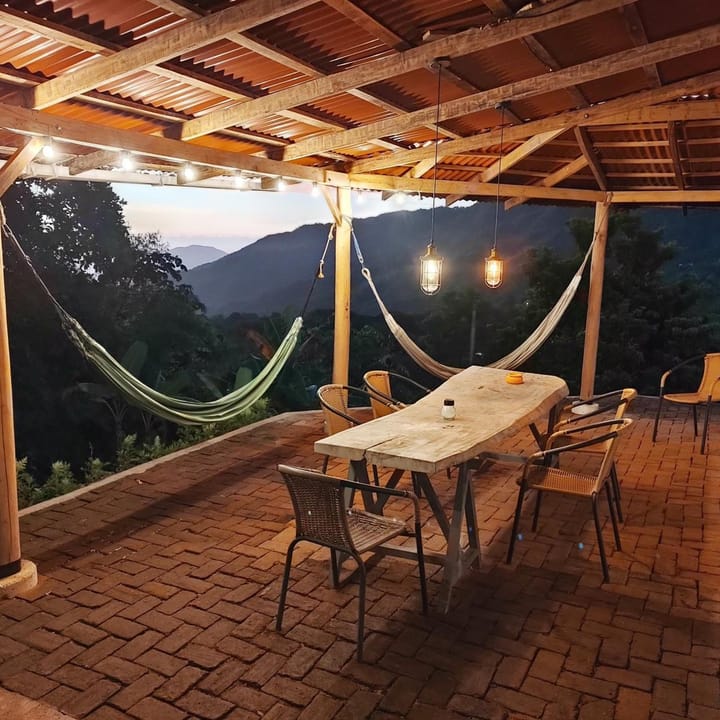 La terraza al anochecer con luces colgantes, hamacas y la mesa larga lista.