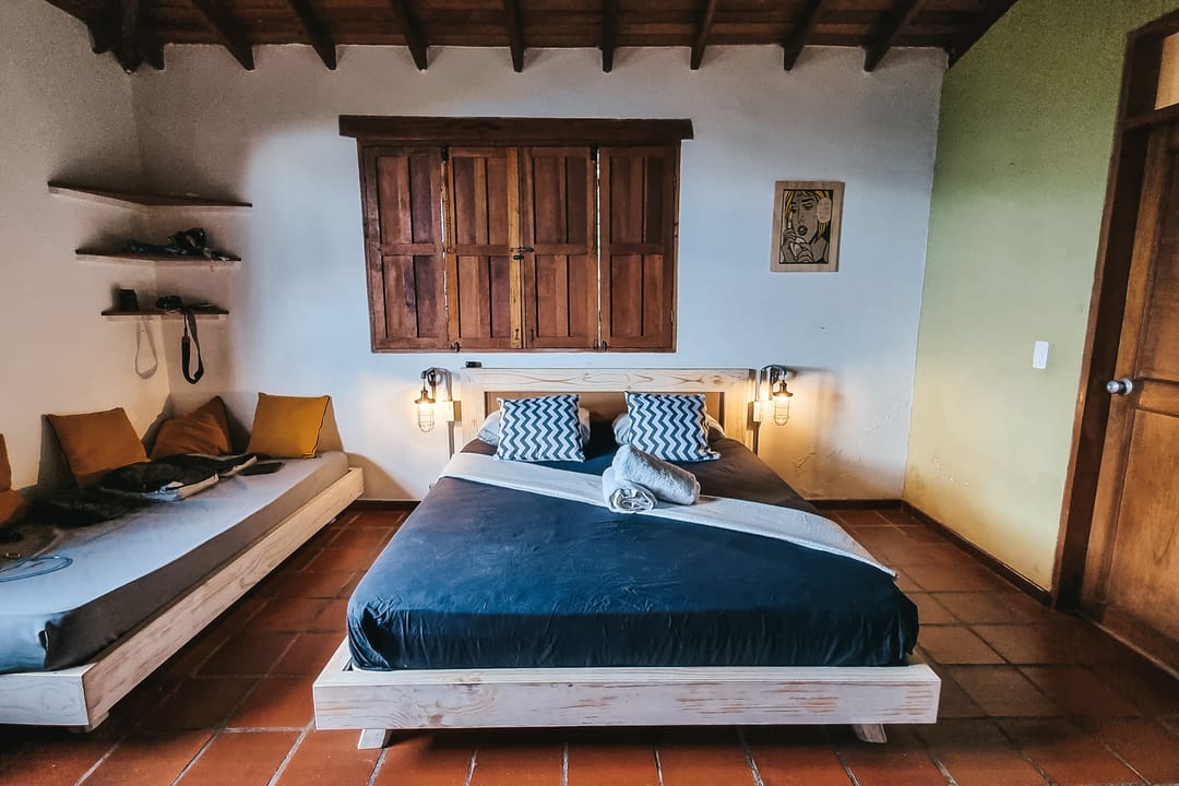 Vista amplia de la habitación doble de Casa Quinta: cama queen, sofá cama, repisas y puerta de madera.