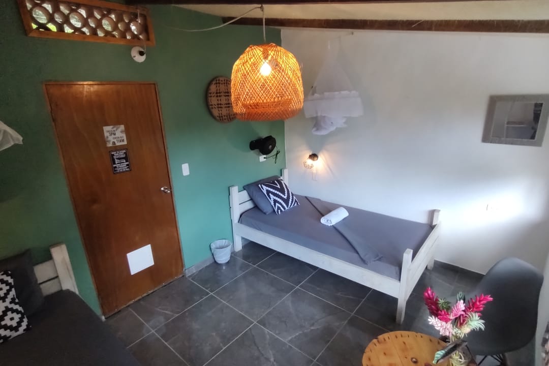 Casa Mango vista hacia la puerta: cama sencilla, cojines y mesita.