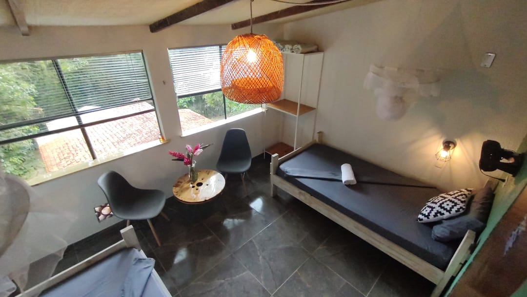 Habitación twin de Casa Mango: dos camas sencillas, ventanales hacia la selva, mesa redonda y sillas.