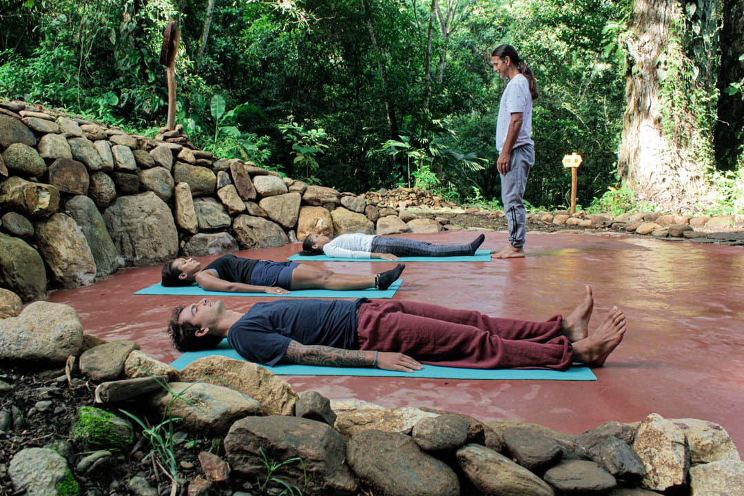 Una sesión de yoga sobre una plataforma de piedra junto al río, bajo los árboles.