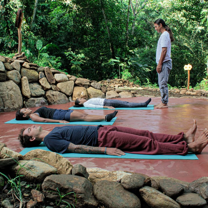 Una sesión de yoga sobre una plataforma de piedra junto al río, bajo los árboles.