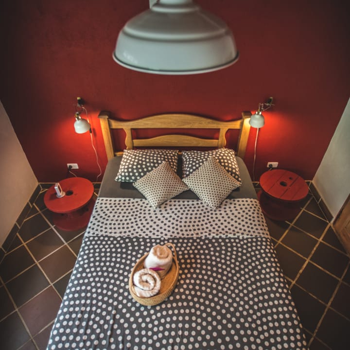 Habitación doble de Casa Maracuyá: pared roja, cama doble con colcha de puntos, lámparas de lectura y lámpara colgante.