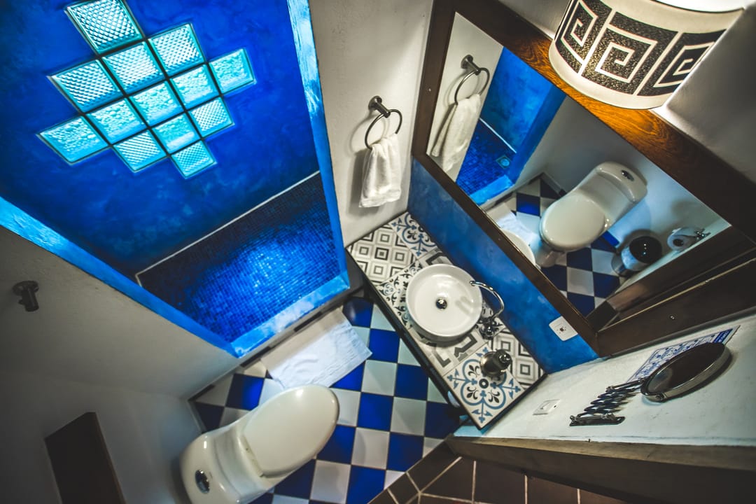 Baño privado con pared de cuadros de vidrio azul, piso de ajedrez y lavamanos.