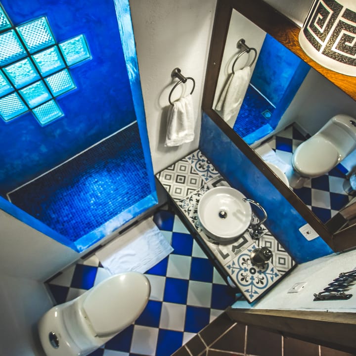 Baño privado con pared de cuadros de vidrio azul, piso de ajedrez y lavamanos.