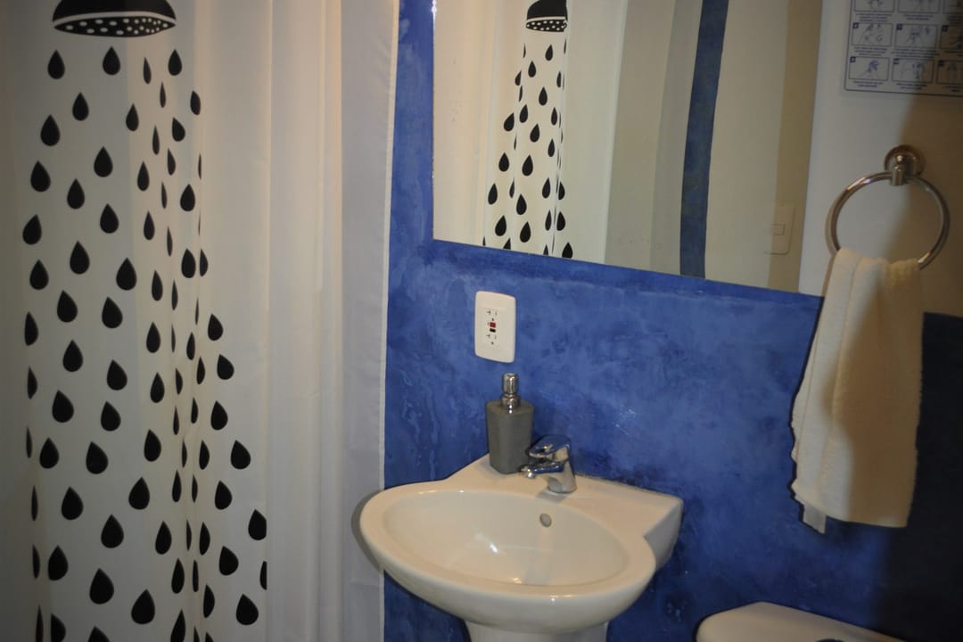 Baño con pared azul, cortina de gotas, lavamanos e inodoro sobre piso de ajedrez.