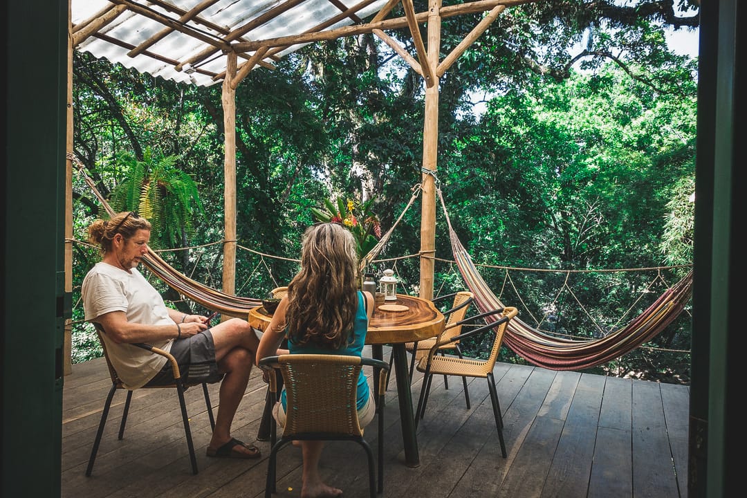 Dos personas conversan en la terraza de madera, con hamacas y selva alrededor.