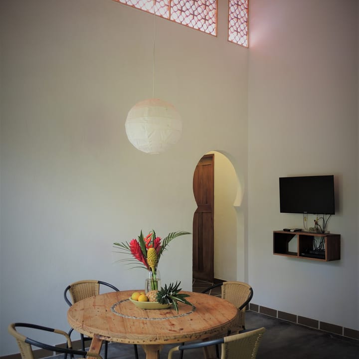 Comedor con mesa redonda, flores de heliconia, televisor y una puerta en arco.