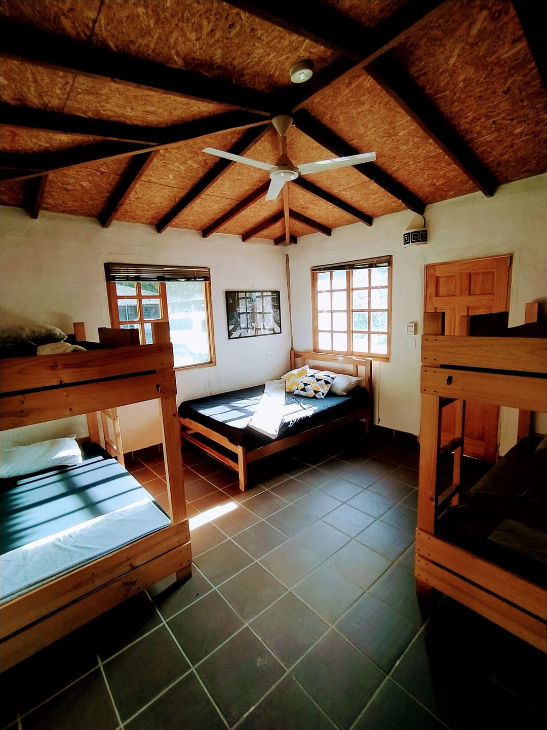 Dormitorio de Casa Quinta: camarotes de madera y una cama sencilla bajo un techo de madera con ventilador.