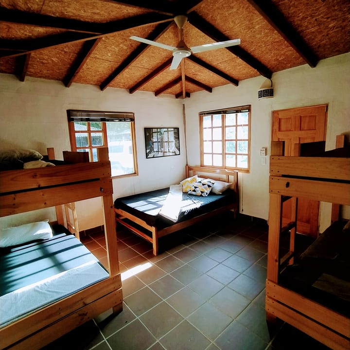 Dormitorio de Casa Quinta: camarotes de madera y una cama sencilla bajo un techo de madera con ventilador.