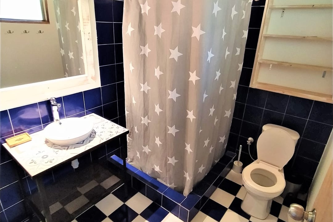 Baño con pared de baldosín azul, piso de ajedrez, cortina de estrellas, lavamanos y espejo.