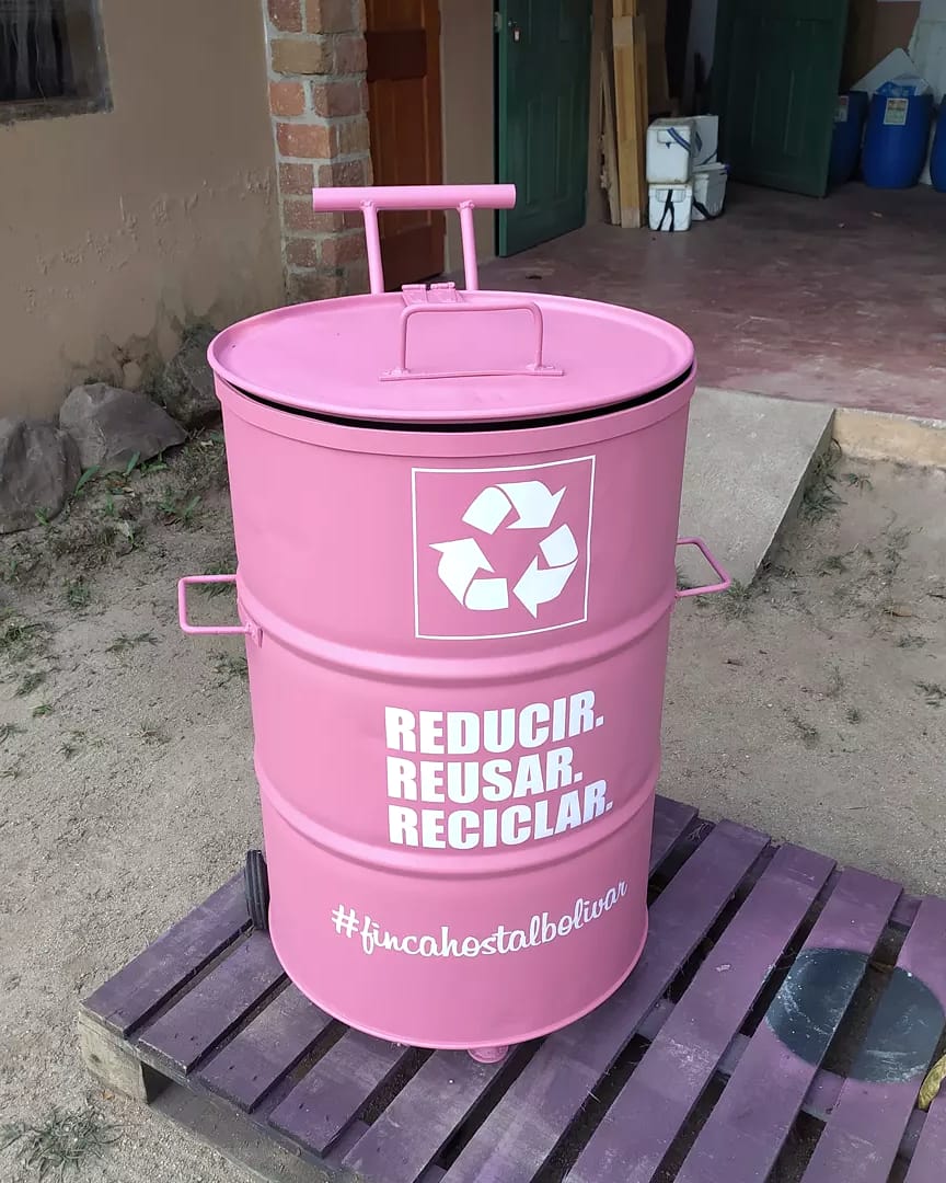 Una caneca rosada hecha con materiales reciclados, pintada con “Reducir, reusar, reciclar”, sobre una estiba de madera.