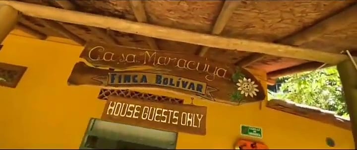 Letrero de madera tallada “Casa Maracuyá · Finca Bolívar” y un aviso “House guests only” sobre una pared amarilla bajo el alero.