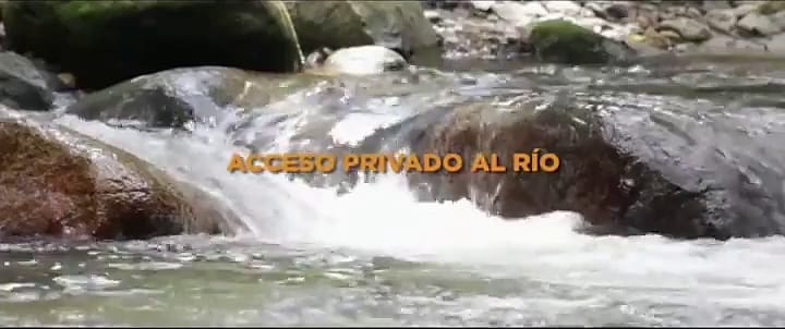 Agua blanca del río bajando entre piedras grandes cubiertas de musgo, con el rótulo “Acceso privado al río” del video original.